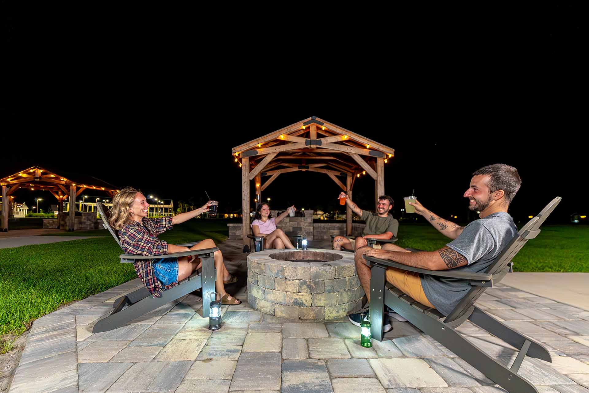Group of friends sitting around a fire pit at night while toasting drinks