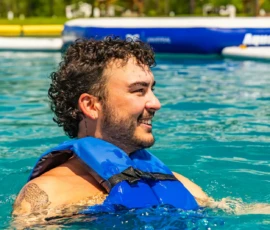 Man in a life jacket in the Island Oaks Swimming Lake in front of the inflatable obstacle course