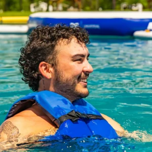 Man in a life jacket in the Island Oaks Swimming Lake in front of the inflatable obstacle course