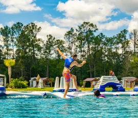 Man in a life jacket running on the inflatable obstacle course on the Island Oaks Swimming Lake