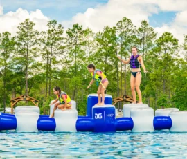 Kids and adults balancing on the Island Oaks inflatable obstacle course on the Swimming Lake