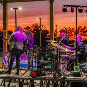 Live band playing outdoors at sunset under an event pavilion at Island Oaks