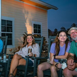 Couples sitting together in rocking chairs with drinks outside an Island Oaks cabin